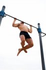 Low angle of muscular male athlete with naked torso doing chin ups on horizontal bar during training on background of gray sky — Stock Photo