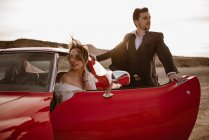 Sposi e sposi riposano vicino a veicoli rossi di lusso durante il viaggio attraverso il Parco Naturale Bardenas Reales in mattinata a Navarra, Spagna — Foto stock