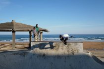 Active skaters riding skateboards and showing tricks in skate park at seaside in summer — Stock Photo