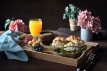 Deliciosos sanduíches de croissant com legumes servidos em bandeja com cappuccino e suco de laranja preparado para o café da manhã francês e colocado em mesa de madeira — Fotografia de Stock