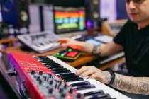 Crop unkenntlich tätowierte männliche Pianist spielt modernen Synthesizer, während Musik am Schreibtisch im Aufnahmestudio komponieren — Stockfoto
