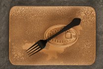 Top view of black fork placed near sealed canned food on rectangular copper tray — Stock Photo