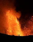 Siluetas de viajeros anónimos de pie contra el humo naranja del volcán activo en Islandia - foto de stock