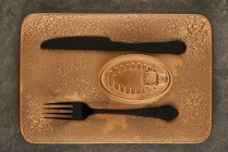 Top view of black fork and knife placed near sealed canned food on rectangular copper tray — Stock Photo
