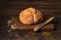Аппетитный ароматный свежеиспеченный домашний хлеб с изюмом, помещенным на деревянную доску, посыпанную травами — стоковое фото