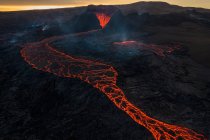 Drone view of stream of hot orange lava flowing through mountainous terrain in morning in Iceland — Stock Photo