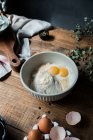 De cima tigela com ovos e creme misturado com migalhas de pão e farinha na mesa de madeira durante a preparação de pastelaria — Fotografia de Stock
