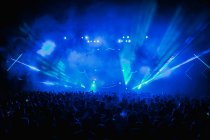 Multidão dançando na moderna sala de concertos em luzes de néon azul durante a performance musical ao vivo — Fotografia de Stock