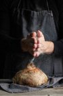 Unrecognizable chef in grembiule in piedi a tavola e decorare pagnotta di pane tradizionale con farina — Foto stock