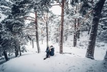 Vue latérale du chien domestique jouant avec la jeune femme sur la neige entre les arbres dans la forêt d'hiver — Photo de stock
