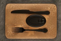 Top view of black fork and knife placed near sealed canned food on rectangular copper tray — Stock Photo