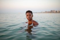 African American female in sea water looking at camera on background of sunset sky — Stock Photo