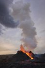 Des éclaboussures de lave orange chaude surgissent du sommet volcanique entouré de fumée en Islande — Photo de stock