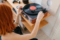 From above side view of crop anonymous female turning on retro record player on shelf in house — Stock Photo