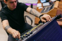 Seitenansicht eines tätowierten männlichen Tontechnikers, der im Tonstudio mit einem Bedienfeld auf dem Audio-Board arbeitet — Stockfoto