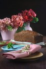 Ainda a vida de um bolo de esponja ao lado de vários vasos rosa com flores em uma mesa — Fotografia de Stock