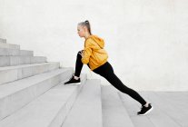 Молодая атлетичная белая женщина, растянувшаяся на улице возле лестницы — стоковое фото