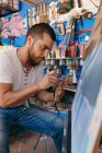 Боковой вид мужчины-художника с помощью аэрозоля для рисования картины на холсте во время работы в творческой мастерской — стоковое фото