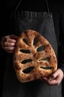 Мужчина-повар в фартуке стоит со свежеиспечённой буханкой хлеба из фугаса — стоковое фото