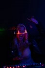 Glückliche Frau hebt den Arm und schreit vor Aufregung, während sie während einer Party in einem dunklen Nachtclub Musik spielt — Stockfoto