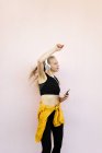 Junge kaukasische Frau trägt Kopfhörer und Sportkleidung, hört Musik am Telefon und tanzt, isoliert auf hellem Hintergrund — Stockfoto