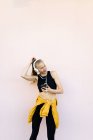 Junge kaukasische Frau trägt Kopfhörer und Sportkleidung, hört Musik am Telefon und tanzt, isoliert auf hellem Hintergrund — Stockfoto
