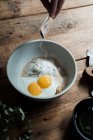 Сверху миска с яйцами и сливками, смешанными с хлебными крошками и мукой на деревянном столе во время приготовления выпечки — стоковое фото