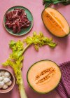 From above exotic melon, mozzarella and prosciutto ingredients for salad preparation on pink colorful background — Stock Photo