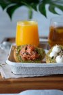 Glasses of juice and herbal tea served on wooden table with assorted healthy avocado toasts with cheese and salmon during breakfast in outdoor cafe — Stock Photo