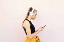 Young caucasian woman wearing headphones and sport outfit, listening to music on the phone, isolated on bright background — Stock Photo