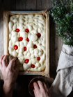 De dessus de personne anonyme décorer la pâte pour de délicieuses focaccia avec des tomates séchées au soleil — Photo de stock