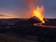 Splashes of hot orange lava erupting from volcanic mountain peak surrounded with smoke in Iceland — Stock Photo