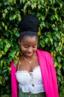 Giovane donna afro-americana alla moda con capelli afro e orecchini alla moda in piedi tra foglie verdi in giardino con gli occhi chiusi — Foto stock