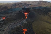 Drohnenblick auf den Strom heißer orangefarbener Lava, der am Morgen durch bergiges Gelände in Island fließt — Stockfoto