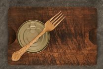 De cima arranhado tábua de corte com garfo e lata selada com alimentos preservados em mesa rústica madeira — Fotografia de Stock