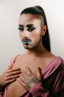 Portrait of glamorous transgender bearded woman in sophisticated make looking at camera against neutral background — Stock Photo
