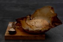 Composition avec pain rond au levain rustique fraîchement cuit sur du papier sulfurisé placé sur du carton en bois avec cuillère et farine de blé — Photo de stock