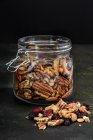 Pot en verre avec noix et fruits secs sur fond rustique foncé — Photo de stock