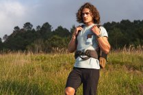 Male backpacker walking in meadow at sundown during trekking in summer and looking away — Stock Photo