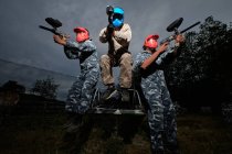 Low angle of teams of paintball players in camouflage outfit and with guns on background of cloudy sky in evening — Stock Photo