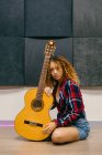 Молодая гитаристка с кудрявыми волосами, опирающаяся на акустическую гитару, глядя в камеру — стоковое фото
