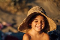 Menina bonito em chapéu de palha sorrindo feliz enquanto descansa na praia no dia ensolarado de verão — Fotografia de Stock