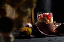 Tazón de batido apetitoso con fresas de granola y arándanos colocados en la mesa cerca de varias flores silvestres - foto de stock