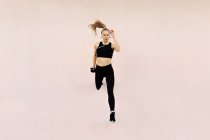 Молода атлетична біла жінка в навушниках і спортивному вбранні, стрибає на яскравому фоні на відкритому повітрі — стокове фото