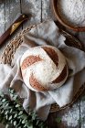 From above homemade fresh sourdough spelt bread on wicker stand with cloth on wooden table with flour scattered — Stock Photo