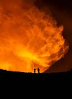Silhouettes of anonymous travelers standing against orange fume of active volcano in Iceland — Stock Photo