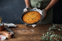 Обрізаний анонімний чоловічий кухар тримає тарілку зі смачним гарбузовим пирогом на пиломатеріалі — стокове фото