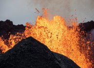 Splashes de lava laranja quente que irrompe do pico da montanha vulcânica cercada de fumaça na Islândia — Fotografia de Stock