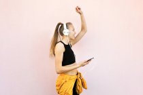 Young caucasian woman wearing headphones and sport outfit, listening to music on the phone and dancing, isolated on bright background — Stock Photo