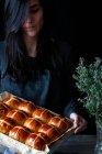 Жінка-пекар, що тримає пух, свіжоспечений гарячий хрест булочки на випічці лотка — стокове фото